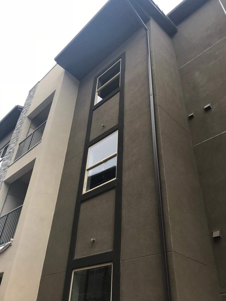 Vertical downspout installed along a multi-story building exterior, demonstrating precision gutter drainage by All Out Gutters.